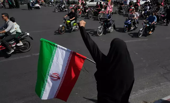 A woman chants slogan as she holds an Iranian flag while motorcyclists ride during a state-organized motorcycle parade called "Janfada," meaning "Sacrifice for Iran,", in Tehran, Iran, Friday, Sept. 25, 2026. (AP Photo/Vahid Salemi)