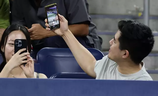 A fan takes a selfie as Elena Rybakina, of Kazakhstan, serves to Jessica Bouzas Maneiro, of Spain, during the second round of the U.S. Open tennis championships, Thursday, Sept. 3, 2026, in New York. (AP Photo/Adam Hunger)