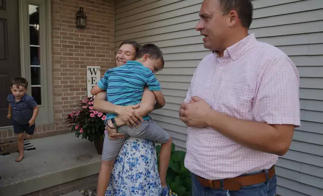 Lizzy Taggart holds her son Fulton, 8, while standing with her husband, Joe, outside their home in Bloomington, Ill., on July 16, 2026. (AP Photo/Jessie Wardarski)
