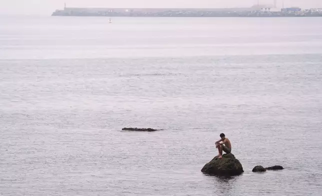 A migrant sits on a rock at El Trampolín beach in the Spanish exclave of Ceuta, Wednesday, Sept. 2, 2026. (AP Photo/Francis González)