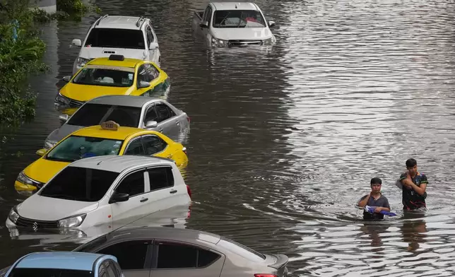 People wade through a flooded street after heavy rain in Bangkok, Thailand, Sunday, Sept. 27, 2026. (AP Photo/Sakchai Lalit)