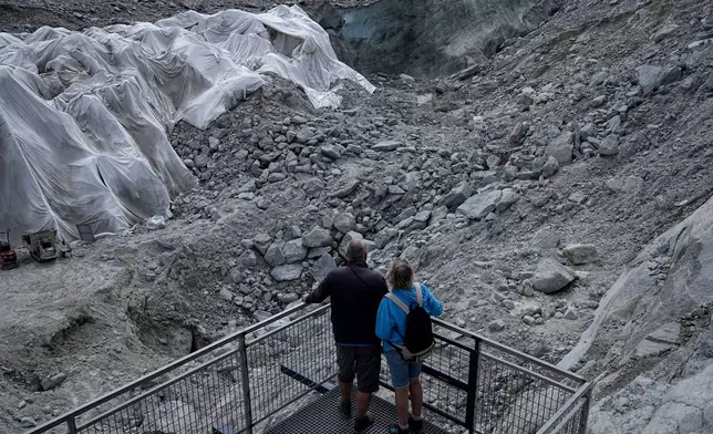 People look at the 'Mer de Glace' glacier as tarpaulins cover the ice cave to prevent it from melting, at the Montenvers station in Chamonix, France, Saturday, Sept. 5, 2026. (AP Photo/Laurent Cipriani)