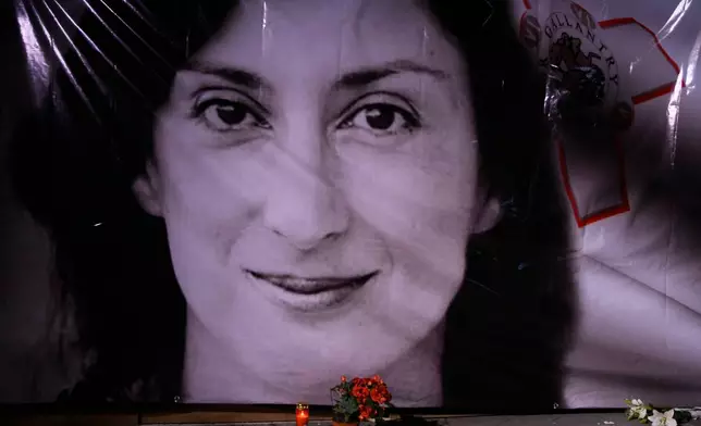 FILE - Flowers and a candle lie in front of a portrait of slain investigative journalist Daphne Caruana Galizia during a vigil outside the law courts in Valletta, Malta, Oct. 16, 2018. (AP Photo/Jonathan Borg, File)