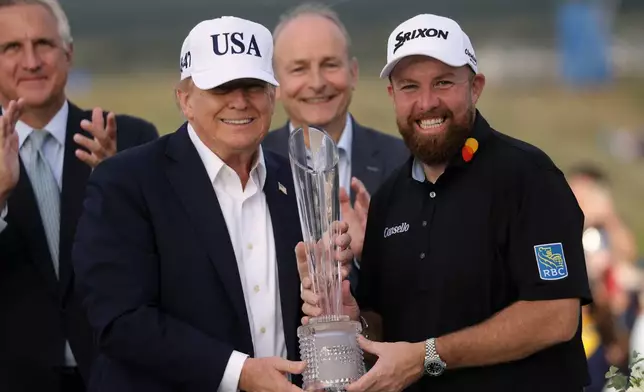 U.S. President Donald Trump presents the trophy to Irish Open golf winner Shane Lowry of Ireland whilst Ireland's Prime Minister Micheal Martin, center rear, looks on, at the Trump International Golf Links course in Doonbeg, Ireland, Sunday, Sept. 13, 2026. (AP Photo/Peter Morrison)