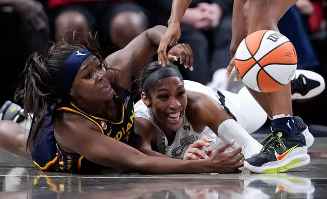 Indiana Fever guard Raven Johnson, left, and Las Vegas Aces center A'ja Wilson, center, go for a loose ball during the first half in Game 2 of a WNBA basketball first-round playoff series in Indianapolis, Tuesday, Sept. 29, 2026. (AP Photo/Michael Conroy)