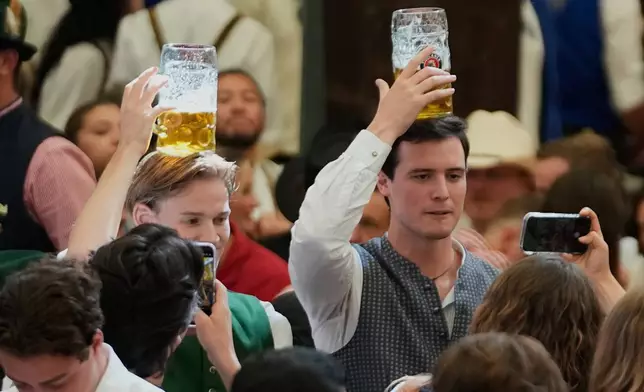 Visitors carry beer mugs on their heads after the opening of the 191st Oktoberfest beer festival in Munich, Germany, Saturday, Sept.19, 2026. (AP Photo/Matthias Schrader)