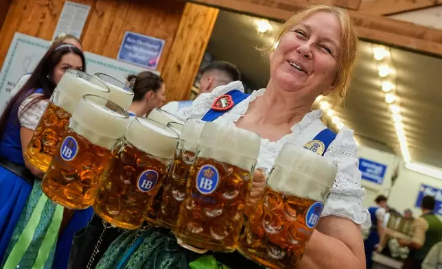 A waitress carries beer mugs after the opening of the 191st Oktoberfest beer festival in Munich, Germany, Saturday, Sept.19, 2026. (AP Photo/Matthias Schrader)
