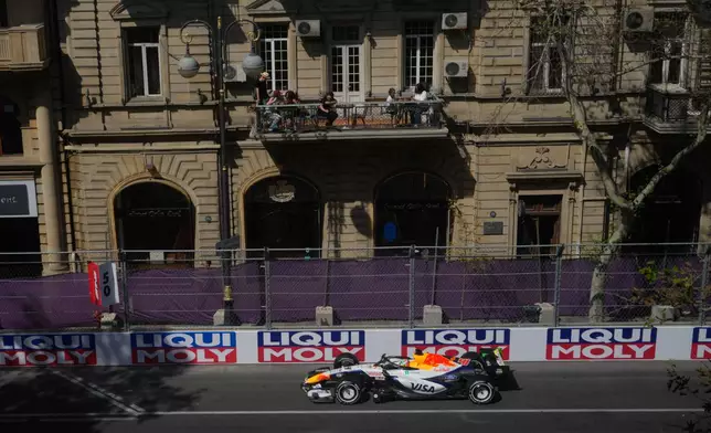People watch from a balcony as Racing Bulls driver Arvid Lindblad of Britain steers his car during the first free practice ahead of the Azerbaijan F1 Grand Prix, in Baku, Azerbaijan, Thursday, Sept. 24, 2026. (AP Photo/Pavel Bednyakov)
