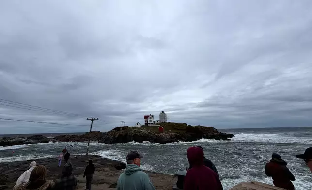 In this photo made with a smartphone, people watch the waves at Nubble Lighthouse in York, Maine, during a nor'easter, Saturday, Sept. 26, 2026. (AP Photo/Caleb Jones)