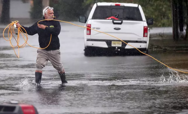 Jose Rosario pulls an extension cord out of his flooded garage to connect to a generator on Catherine St. Saturday, Sept. 26, 2026, in Long Branch, N.J. (AP Photo/Noah K. Murray)