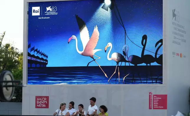People gather in front of a billboard prior to the 83rd edition of the Venice Film Festival in Venice, Italy, on Monday, Aug. 31, 2026. (Photo by Alessandra Tarantino/Invision/AP)