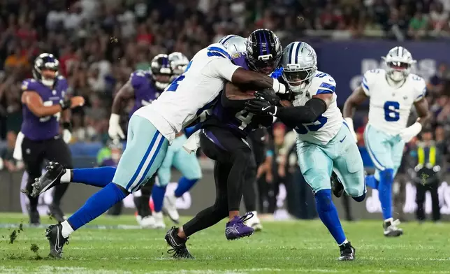 Baltimore Ravens wide receiver Zay Flowers (4) is tackled by Dallas Cowboys safety Markquese Bell (14) and linebacker Dee Winters (53) during the first half of an NFL football game in Rio de Janeiro, Sunday, Sept. 27, 2026. (AP Photo/Andre Penner)