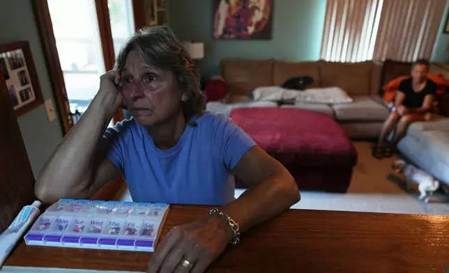 Kate Koubek, foreground, pauses after talking about her wife's terminal illness in front of a pill organizer containing medications for Deb Robertson, right, in the living room of their home in Lombard, Ill., on Tuesday, Sept. 8, 2026. (AP Photo/Luis Andres Henao)
