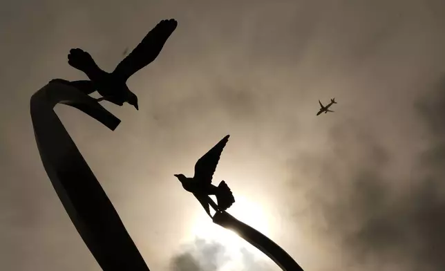 A plane flies above a sculpture of ascending doves at a memorial for survivors and lives lost to suicide dedicated by the Archdiocese of Chicago at Queen of Heaven Catholic Cemetery in Hillside, Ill., on Wednesday, Sept. 9, 2026. (AP Photo/Luis Andres Henao)