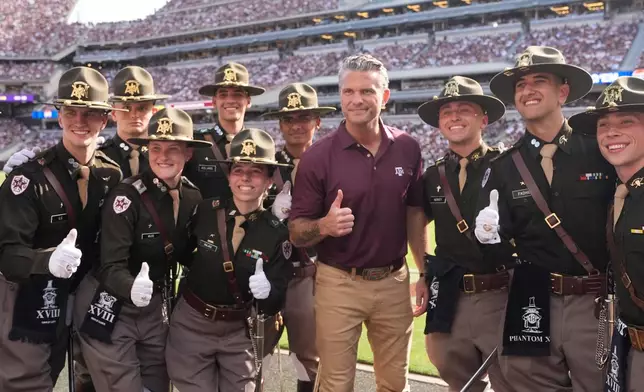 U.S. Secretary of Defense Pete Hegseth, center, poses with members of the Texas A&M Corps of Cadets on the sideline during the second half of an NCAA college football game against Kentucky, Saturday, Sept. 19, 2026, in College Station, Texas. (AP Photo/David J. Phillip)