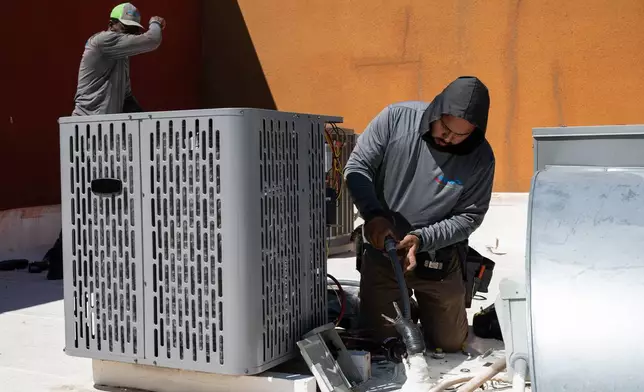 FILE - Sonel Telemaque, left, wipes sweat from his brow while installing a new air conditioning unit alongside Brian Hermosillo during record-breaking heat, March 19, 2026, in Tempe, Ariz. (AP Photo/Caitlin O'Hara, File)