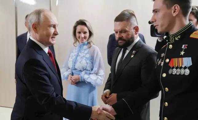 FILE - Russian President Vladimir Putin, left, greets Vladislav Golovin, right, during a meeting with the leaders of the United Russia political party as Presidential Commissioner for Children's Rights Maria Lvova-Belova, center, and military correspondent Yevgeny Poddubny, second right, in Moscow on Saturday, Sept. 5, 2026. (Gavriil Grigorov/Sputnik, Kremlin Pool Photo via AP, File)