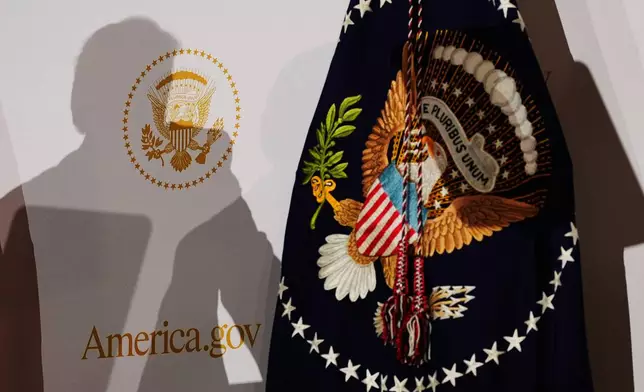 The shadow of President Donald Trump is cast on a backdrop bearing the presidential seal and the America.gov logo beside the presidential flag as he speaks at the Andrew W. Mellon Auditorium, Tuesday, Sept. 29, 2026, in Washington. (AP Photo/Alex Brandon)