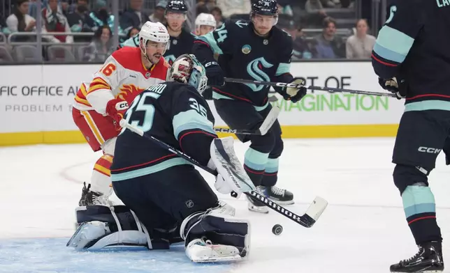Seattle Kraken goaltender Joey Daccord (35) goes for the puck as Calgary Flames center Morgan Frost (16) tries to score during the second period of an NHL hockey game Sunday, Oct. 4, 2026, in Seattle. (AP Photo/Jason Redmond)