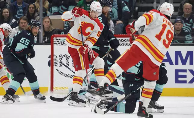 Calgary Flames right wing Matvei Gridin (92) sets a screen as defenseman Zayne Parekh (19) moves the puck and Seattle Kraken defenseman Ryan Lindgren (55) defends during the first period of an NHL hockey game Sunday, Oct. 4, 2026, in Seattle. (AP Photo/Jason Redmond)