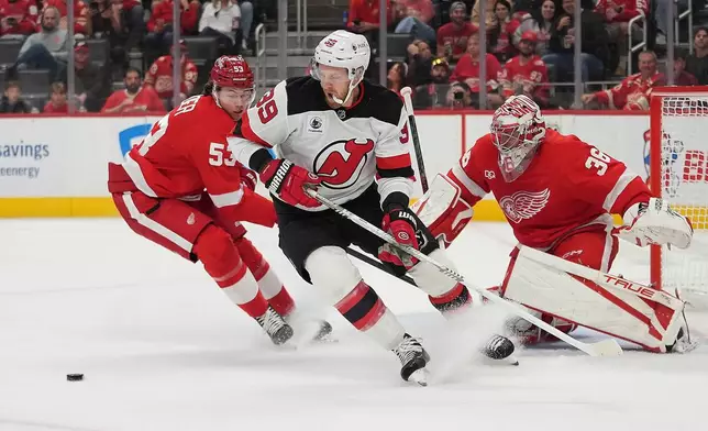 New Jersey Devils right wing Anthony Mantha (39) and Detroit Red Wings defenseman Moritz Seider (53) chase the puck as John Gibson (36) watches in the first period of an NHL hockey game Tuesday, Oct. 13, 2026, in Detroit. (AP Photo/Paul Sancya)