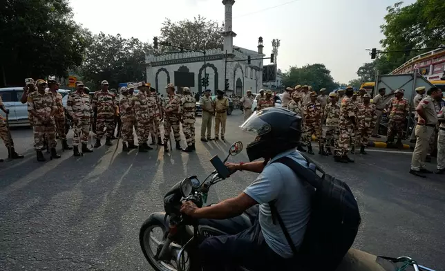 A motorcyclist drives past security personnel guarding as members of the student wing of India's Congress party and other protesters march demanding the resignation of the country's election chief Gyanesh Kumar, in New Delhi, India, Thursday, Oct. 8, 2026. (AP Photo/Manish Swarup)