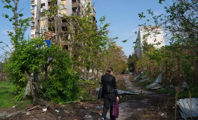 A woman walks in front of a residential building damaged in a Russian attack during a local ceasefire related to a humanitarian aid mission in Oleshky, in Kherson, Ukraine, Wednesday, Oct. 28, 2026. (AP Photo/Evgeniy Maloletka)