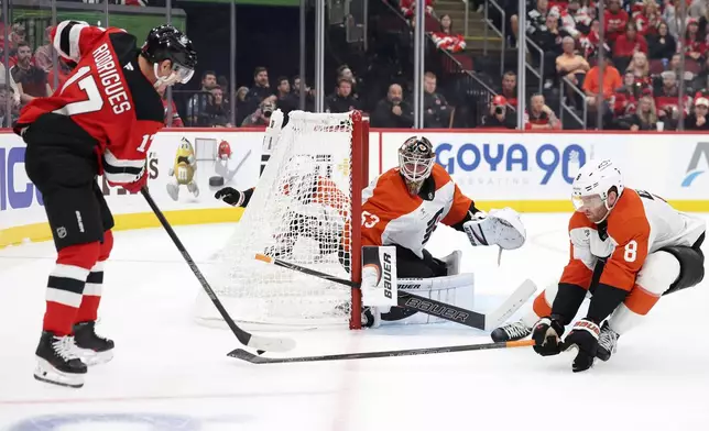 New Jersey Devils center Evan Rodrigues (17) has his shot defended by Philadelphia Flyers defenseman Cam York (8) in front of Flyers goaltender Joseph Woll (53) during the second period of an NHL hockey game Thursday, Oct. 1, 2026, in Newark, N.J. (AP Photo/Adam Hunger)