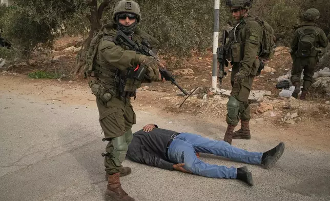 Israeli soldiers stand beside a wounded Palestinian man lying on a road after they shot him following a settler attack on Palestinians harvesting olives in the West Bank village of Abu Falah, Friday, Oct. 16, 2026. (AP Photo/Leo Correa)