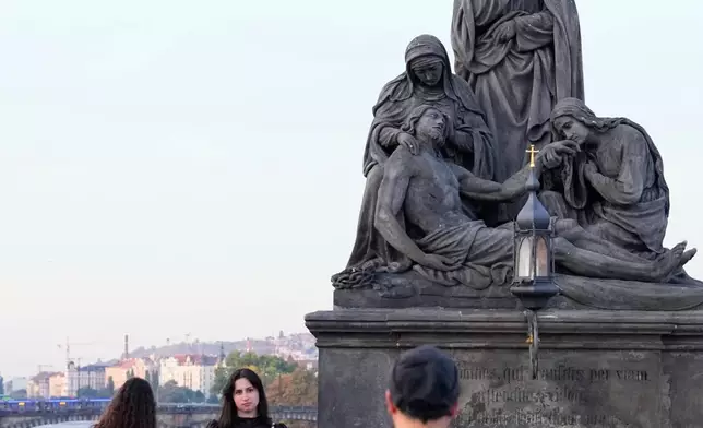 People pose to recreate a famous photo of two members of Depeche Mode, taken by Dutch photographer Anton Corbijn in 1988, by the Pieta statue at the Charles Bridge in Prague, Czech Republic, Friday, Oct. 2, 2026. (AP Photo/Petr David Josek)
