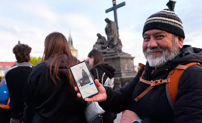 Jorge Sanchez from Los Angeles displays a famous photo of two members of Depeche Mode, taken by Dutch photographer Anton Corbijn in 1988, as he waits in line to recreate this image by the Pieta statue at the Charles Bridge in Prague, Czech Republic, Thursday, Sept. 24, 2026. (AP Photo/Petr David Josek)