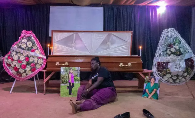 Cousin of domestic violence victim Achiah Geraldine sits on the floor beside her portraits and the casket during a wake inside a community hall in Yaoundé, Cameroon, Friday, Sept. 18, 2026. (AP Photo/Angel Ngwe)