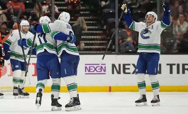 Teammates celebrate with Vancouver Canucks defenseman Filip Hronek (17) after his goal during overtime in an NHL hockey game against the Anaheim Ducks Tuesday, Oct. 27, 2026, in Anaheim, Calif. (AP Photo/Gregory Bull)