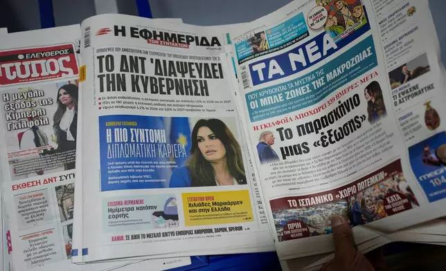 A mini-market owner arranges newspapers carrying front-page headlines about the resignation of U.S. Ambassador to Greece Kimberly Guilfoyle, with the headline of Efsyn, at center describing it as "the shortest diplomatic career," in Athens, Greece, Wednesday, Oct. 14, 2026. (AP Photo/Thanassis Stavrakis)