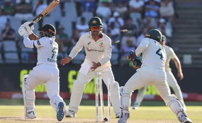 South Africa's captain Temba Bavuma, left, is bowled out by Australia's Nathan Lyon, as teammates Travis Head, center, and Alex Carey look on, on day three of the third cricket test match between South Africa and Australia, in Cape Town, South Africa, Thursday, Oct. 29, 2026. (AP Photo/Halden Krog)