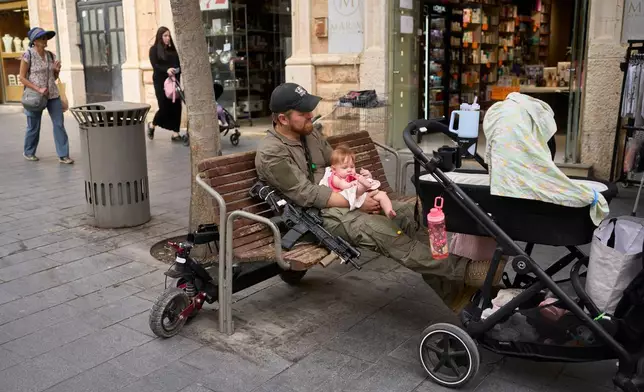 An Israeli soldier sits on a bench holding a baby in Jerusalem, Monday, Oct. 12, 2026. (AP Photo/Ohad Zwigenberg)