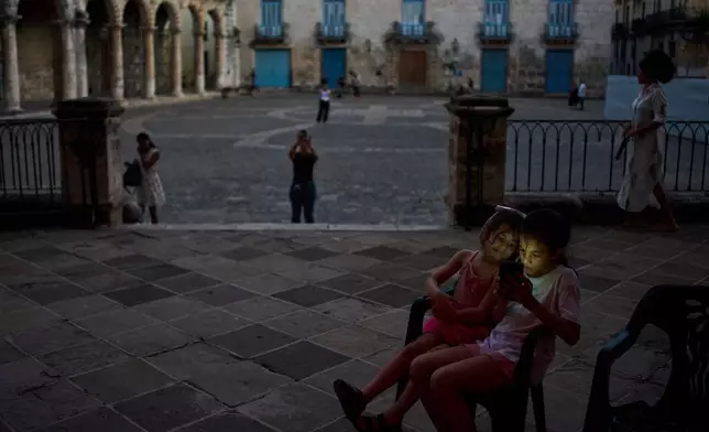 Two girls look at a cellphone screen while sitting in Cathedral Square in Havana, Cuba, Tuesday, Oct. 13, 2026. (AP Photo/Ramon Espinosa)