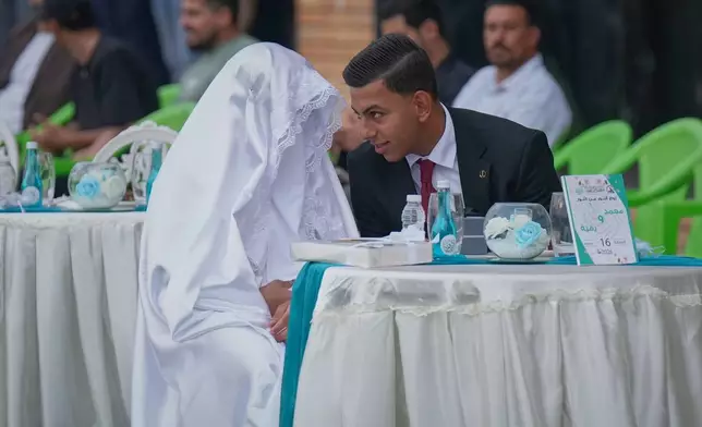 A groom leans toward his bride to speak during a mass wedding organized by the Popular Mobilization Forces for children of fallen and wounded fighters and couples from low-income families in Baghdad, Iraq, Friday, Oct. 16, 2026. (AP Photo/Hadi Mizban)