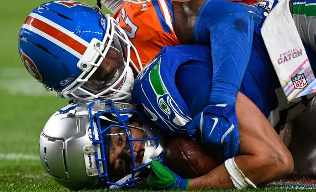 Seattle Seahawks wide receiver Jaxon Smith-Njigba is tackled by Denver Broncos cornerback Jahdae Barron (23) during overtime in an NFL football game in Denver, Thursday, Oct. 15, 2026. (AP Photo/Geneva Heffernan)