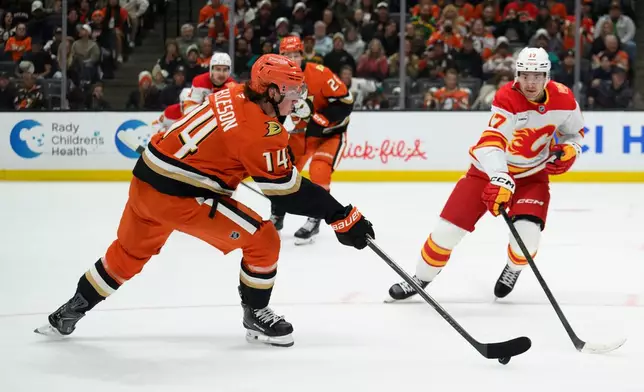 Anaheim Ducks defenseman Drew Helleson (14) shoots as Calgary Flames center Yegor Sharangovich (17) defends during the second period of an NHL hockey game, Tuesday, Oct. 13, 2026, in Anaheim, Calif. (AP Photo/Kyusung Gong)