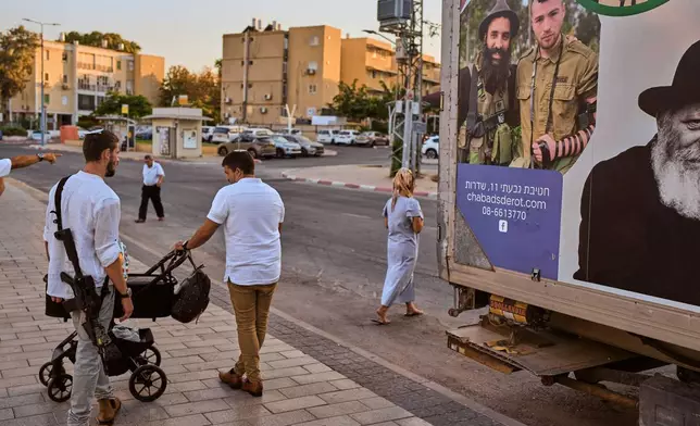 Israelis stand on the sidewalk outside a police station where a memorial stands for victims of the Oct. 7 attack by Hamas three years prior, in Sderot, southern Israel, Saturday, Oct. 3, 2026. (AP Photo/Oded Balilty)