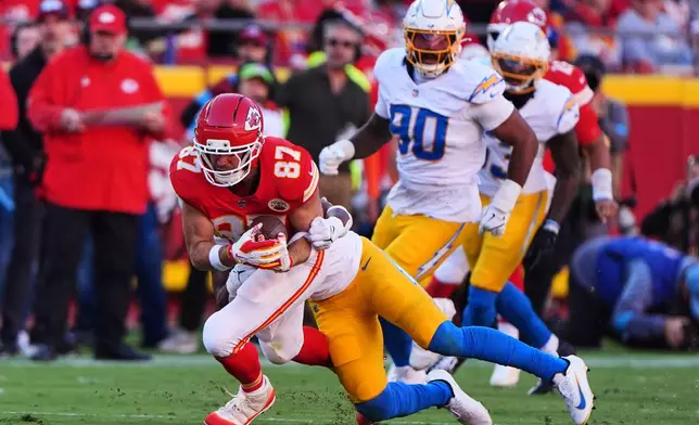 Kansas City Chiefs tight end Travis Kelce (87) catches a pass and is tackled by Los Angeles Chargers linebacker Daiyan Henley, rear, during the first half of an NFL football game in Kansas City, Mo., Sunday, Oct. 18, 2026. (AP Photo/Charlie Riedel)