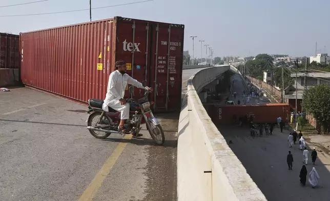 People use an available passage on a road barricaded with shipping containers by authorities to maintain law and order situation following the Pakistani president declared a state of emergency in northwestern Khyber Pakhtunkhwa province and suspended its government, in Peshawar, Pakistan, Monday, Oct. 12, 2026. (AP Photo/Muhammad Zubair)