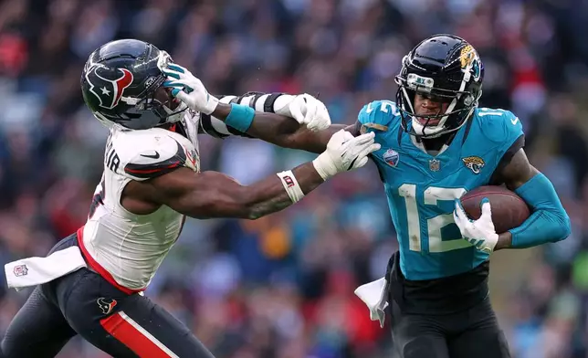 Jacksonville Jaguars wide receiver Travis Hunter (12) holds off Houston Texans linebacker Azeez al-Shaair (0) during an NFL football game in London, Sunday, Oct. 18, 2026. (AP Photo/Ian Walton)