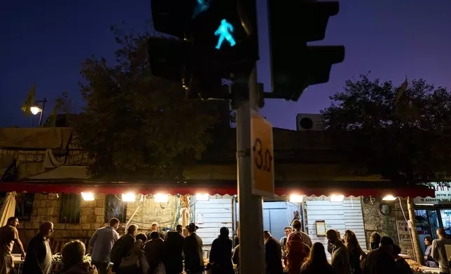 Customers gather around a produce stall at dusk in Jerusalem, Wednesday, Oct. 21, 2026. (AP Photo/David Goldman)