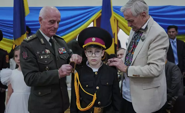 Ukrainian Army General Volodymyr Lishavsky and actor Volodymyr Talashko attach shoulder straps to a young cadet during the initiation ceremony at a cadet lyceum in Kyiv, Friday, Oct. 23, 2026. (AP Photo/Efrem Lukatsky)