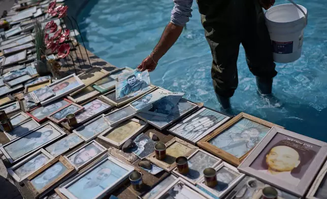 A worker picks up a photo of Staff Sgt. Matan Vinogradov who was killed in combat in 2024 after it fell into a fountain decorated with photos of victims of the Hamas attacks and soldiers who died in the war at Dizengoff Square in central Tel Aviv, Thursday, Oct. 22, 2026. (AP Photo/David Goldman)