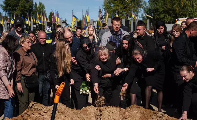 Illia Honcharenko's mother and other family members scatter three handfuls of earth in a final farewell to the 14-year-old, who was killed in a Russian missile strike on a residential building on Sept. 30, during his funeral in Vyshhorod, Kyiv region, Ukraine, Friday, Oct. 2. (AP Photo/Evgeniy Maloletka)