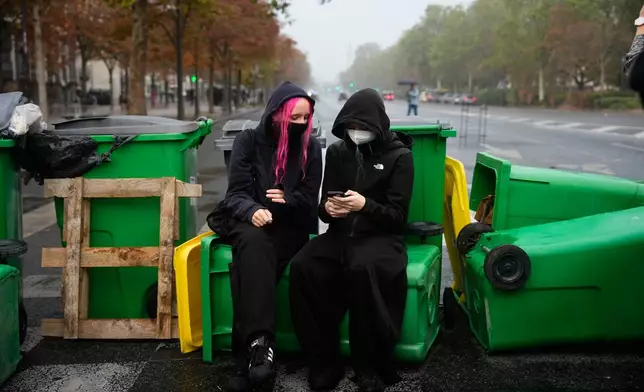 A student checks her smartphone in front of the Helene Boucher high school blockaded with garbage bins during a protest against under-resourced schools in Paris, Tuesday, Oct. 13, 2026. (AP Photo/Teresa Suarez)