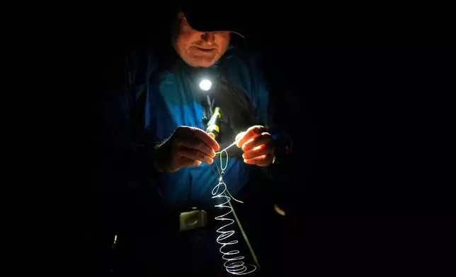 Fishing guide Bill Wetzel ties on a new leader for a client while fishing on a dark night during the new moon Friday, Oct. 9, 2026, in Montauk, N.Y. (AP Photo/Robert F. Bukaty)